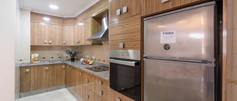 A modern kitchen with wooden cabinets, a stainless steel refrigerator, and a built-in oven.
