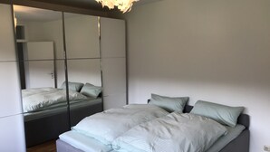 A modern bedroom with a large mirror, a bed with light-colored bedding, and a wooden floor.