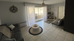 Un salon comprenant un canapé, une table basse, un téléviseur et un balcon avec une porte coulissante.