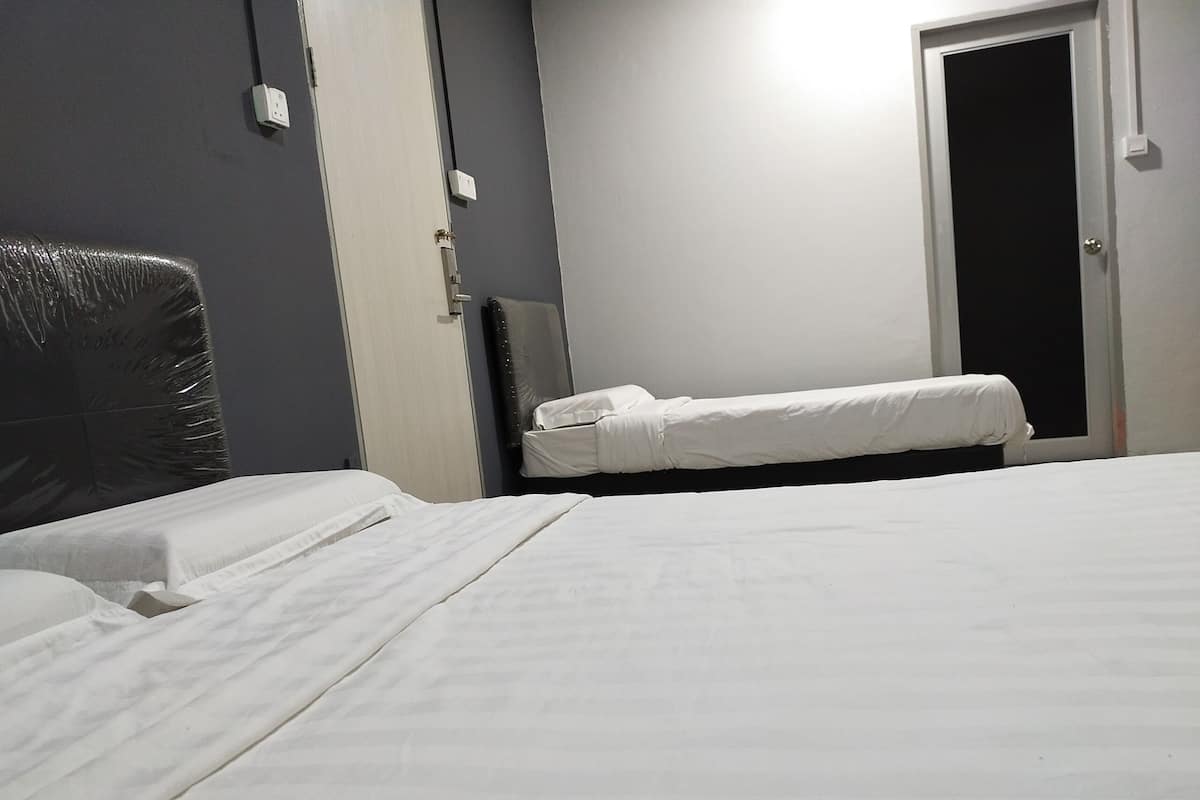 A hotel room with two beds, a dark-colored headboard, a small bedside table, and a door with a light switch.