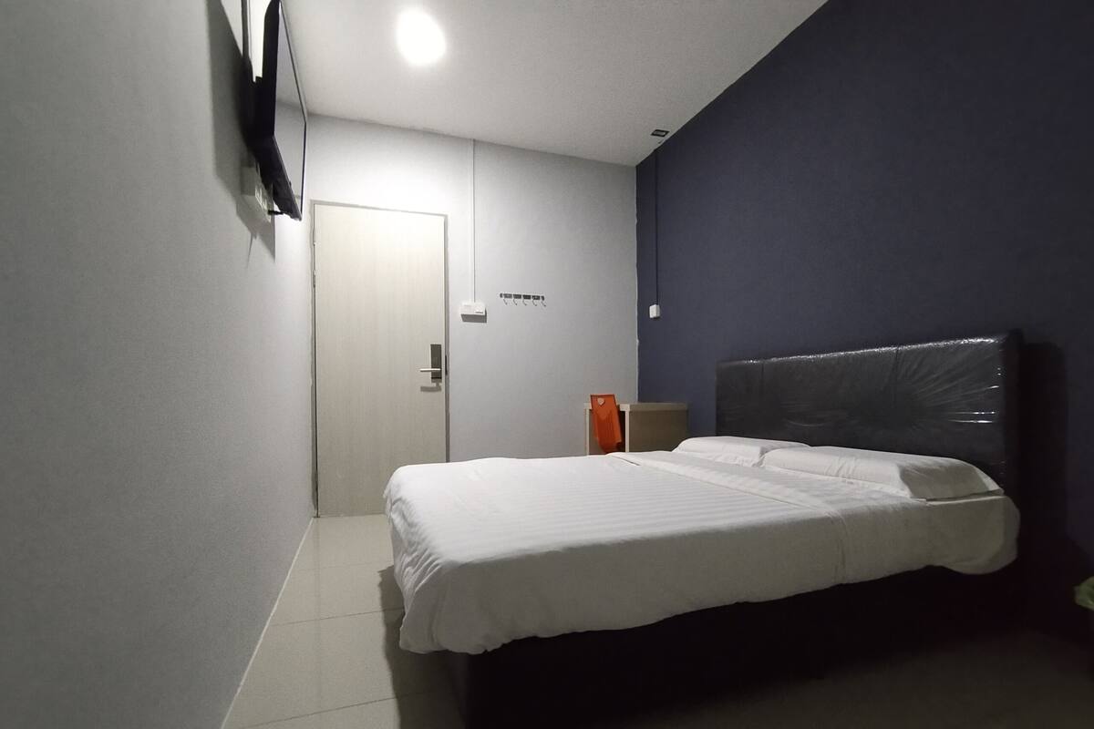 A hotel room with a bed, a nightstand, a wall-mounted TV, and a door.