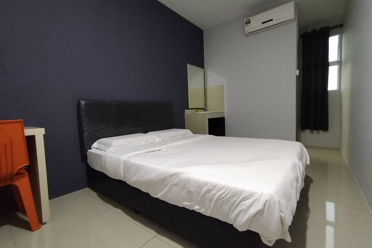 A hotel room with a single bed, a desk, a chair, and a window with curtains.