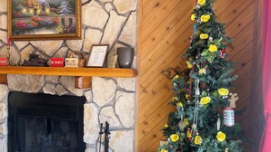 A fireplace with a stone mantle, a Christmas tree with yellow flowers, and a framed painting above the mantle. - Yellow Rose of Red River - In town, WIFI (Red River)