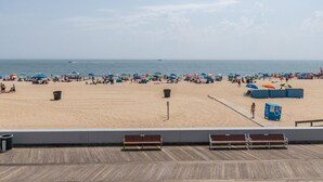 Una playa con una terraza de madera en primer plano, una extensión de arena en el centro y el océano al fondo.