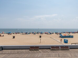 Ein Strand mit einer Holzterrasse im Vordergrund, einem sandigen Ufer in der Mitte und dem Meer im Hintergrund.