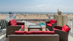 Una terraza con mobiliario de mimbre y cojines rojos, con vista a una playa con sombrillas y gente.