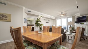 Un comedor con mesa y sillas de madera, un ventilador de techo y vista al salón.