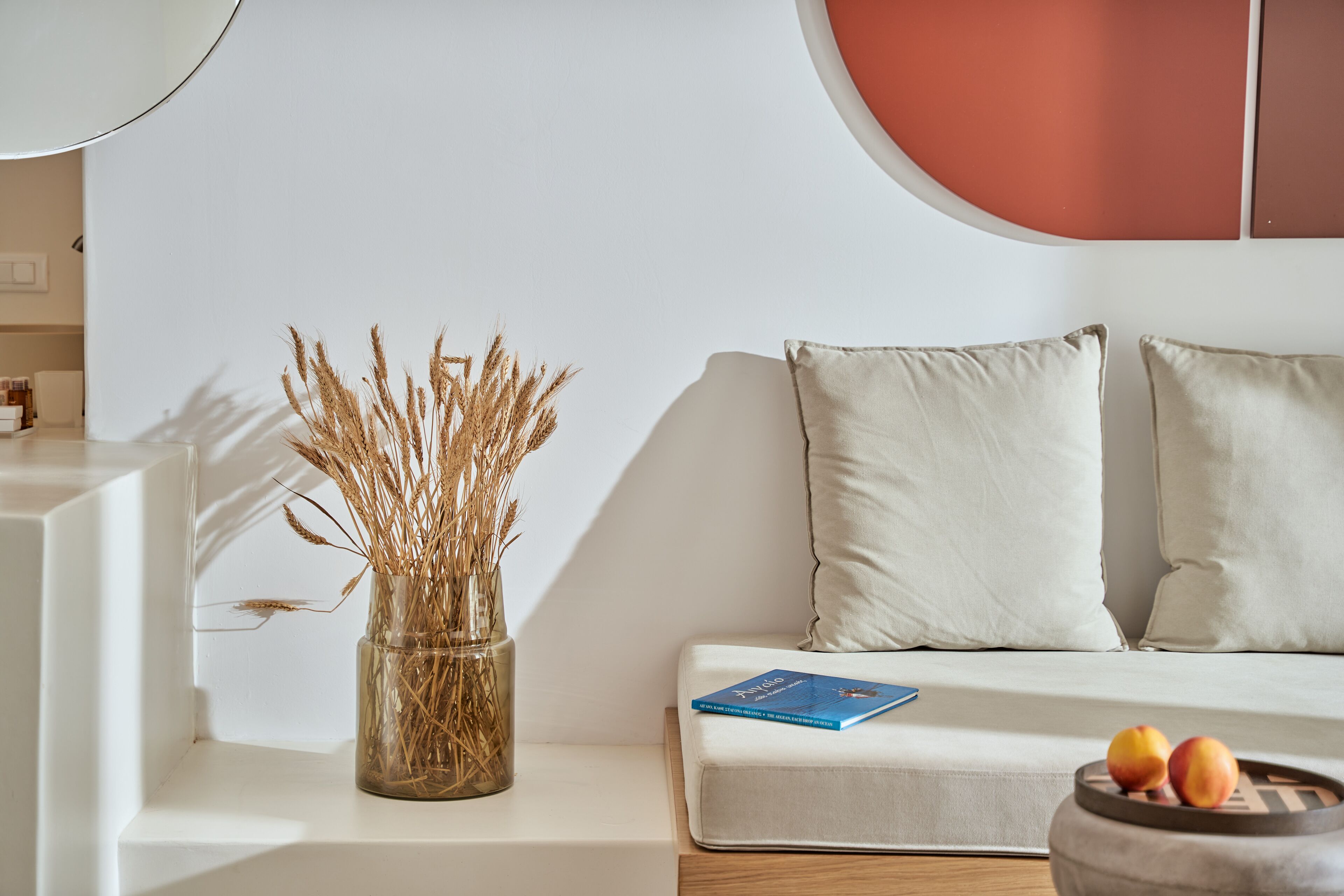 A modern living room with a white sofa, a vase with dried plants, and a book on the sofa.