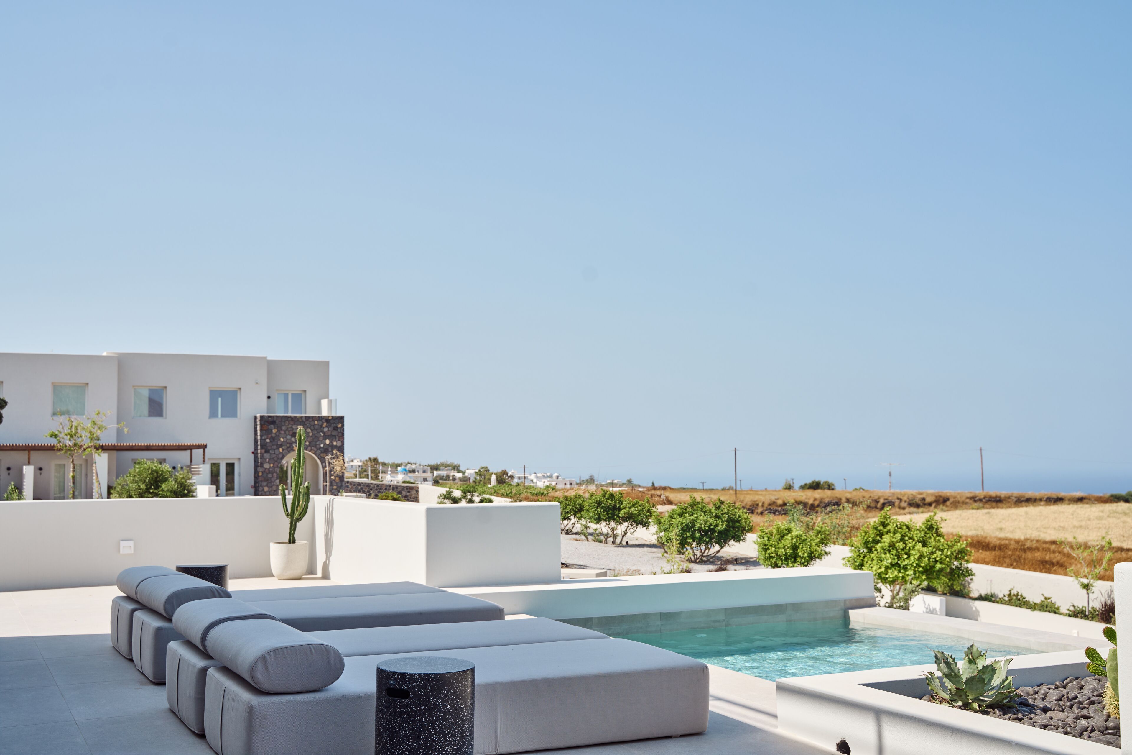 A modern outdoor pool area with a minimalist pool design, a seating area with cushions, and a view of the sea.