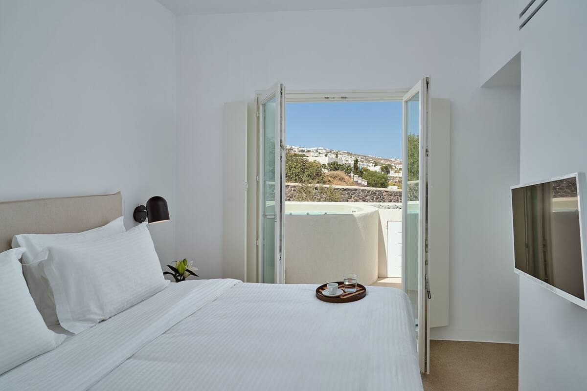 A hotel room with a bed, a tray with a cup and a glass, a TV, and a view of a hillside.