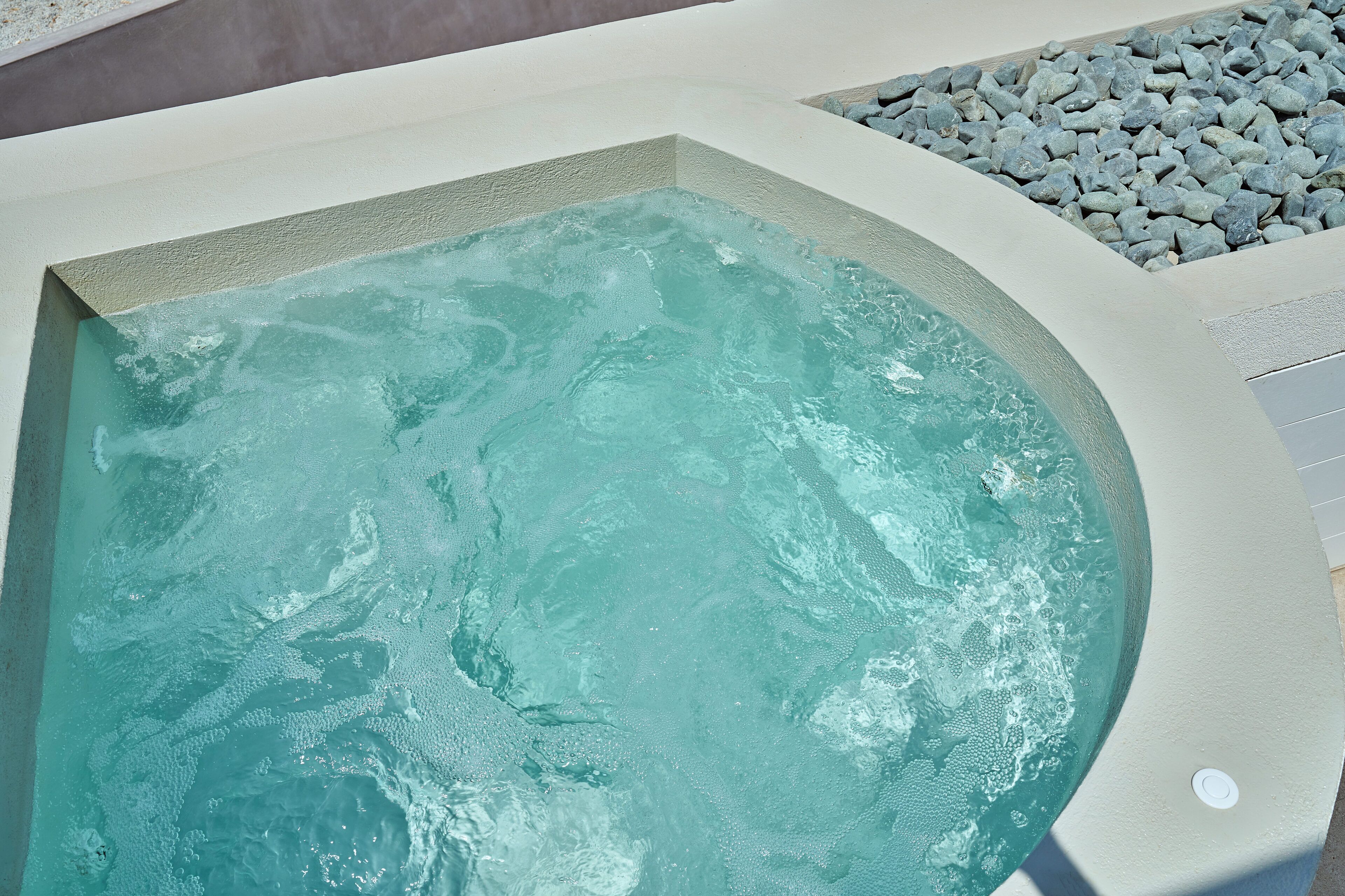 A spa pool with clear water, surrounded by a white pool deck and a pebble area.