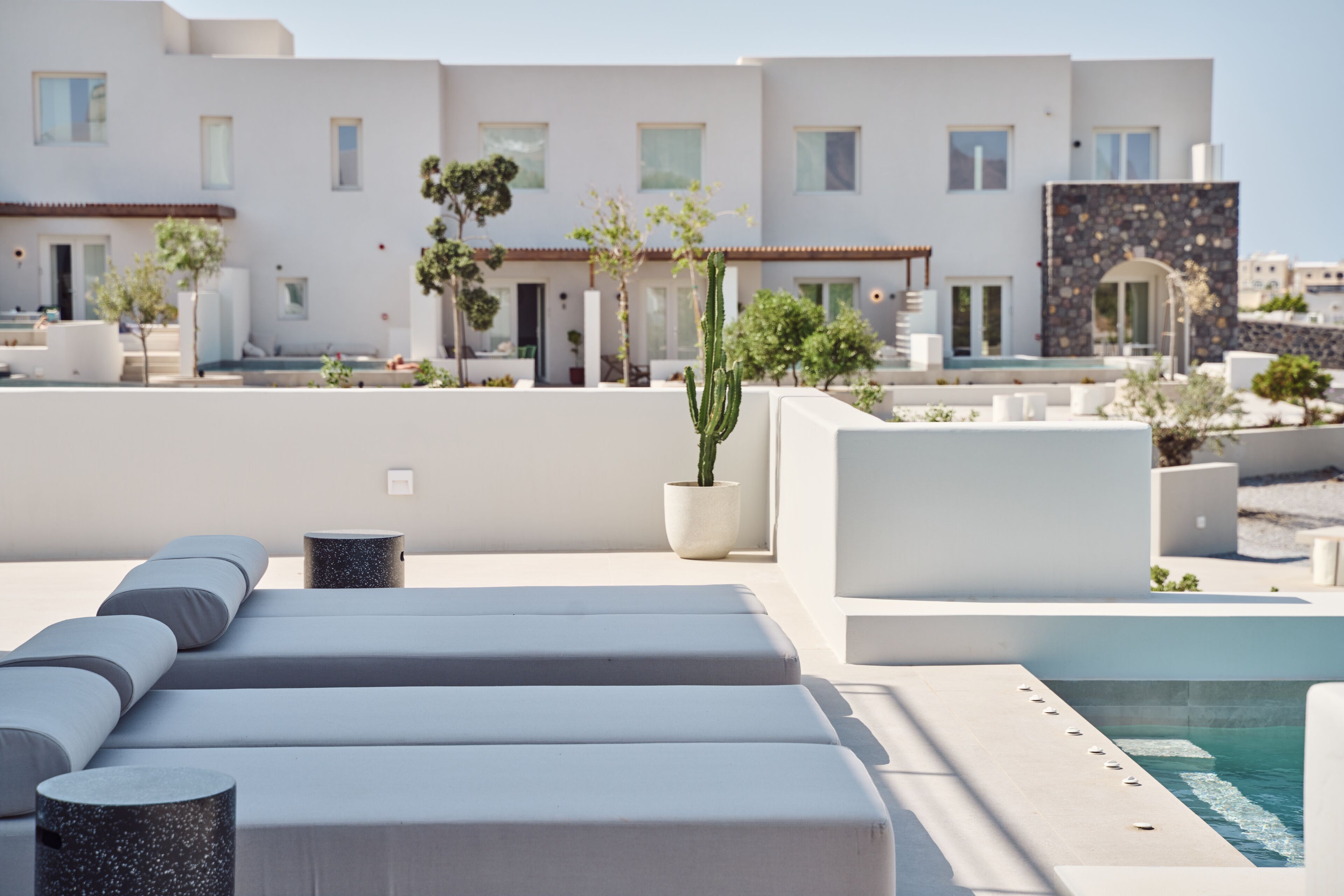 A rooftop terrace with modern outdoor seating, a pool, and a view of a white building with multiple windows.