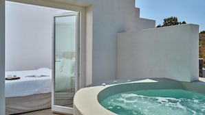 A modern bathroom with a bathtub, a glass shower enclosure, and a bed with white linens. - Lilium Homes (Santorini)