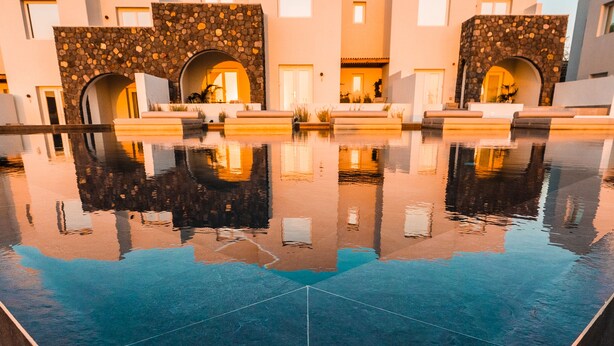 A modern hotel with a reflective pool, stone archways, and a clear blue sky. - Lilium Homes (Santorini)