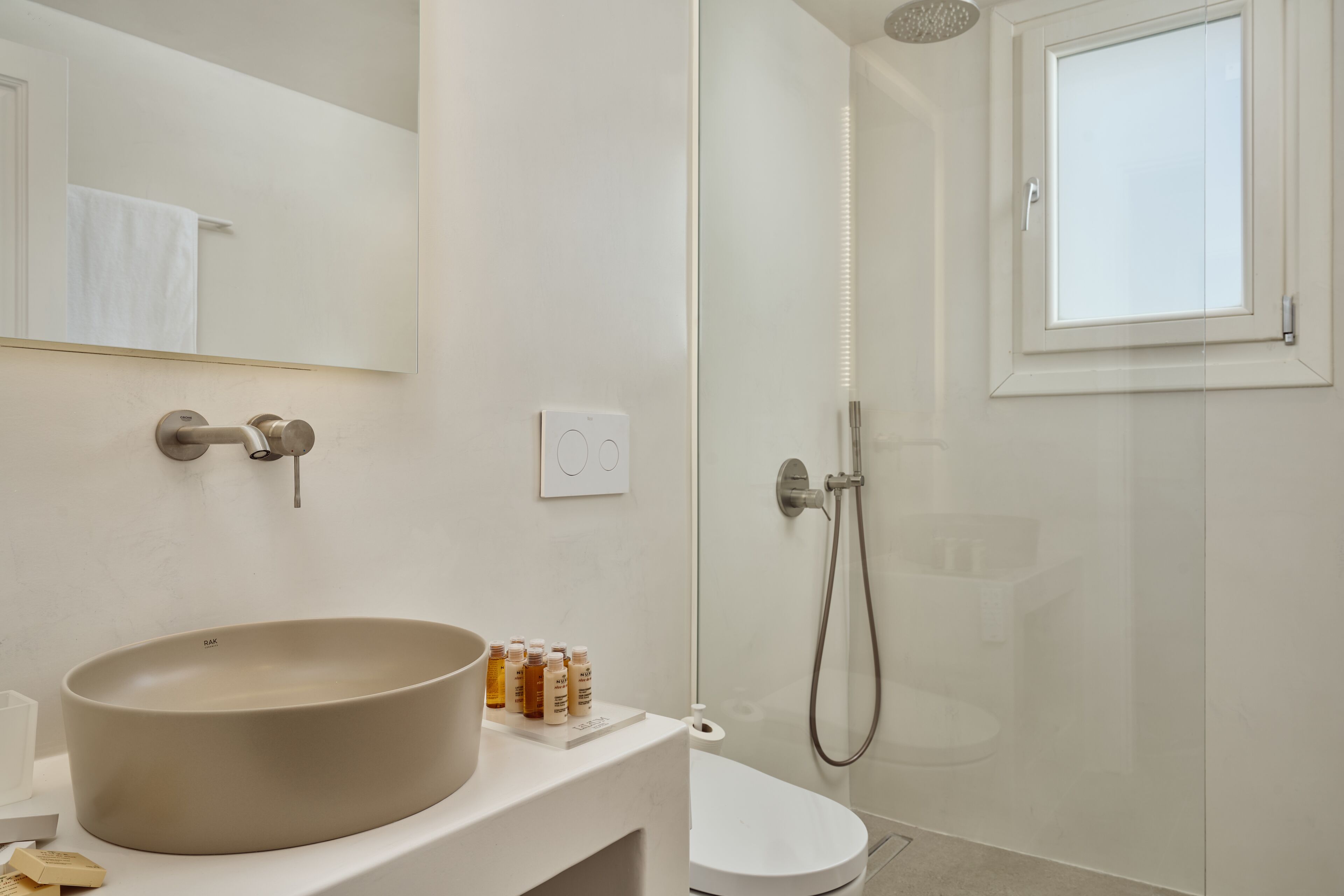 A modern bathroom with a large oval sink, a glass shower enclosure, and a window.