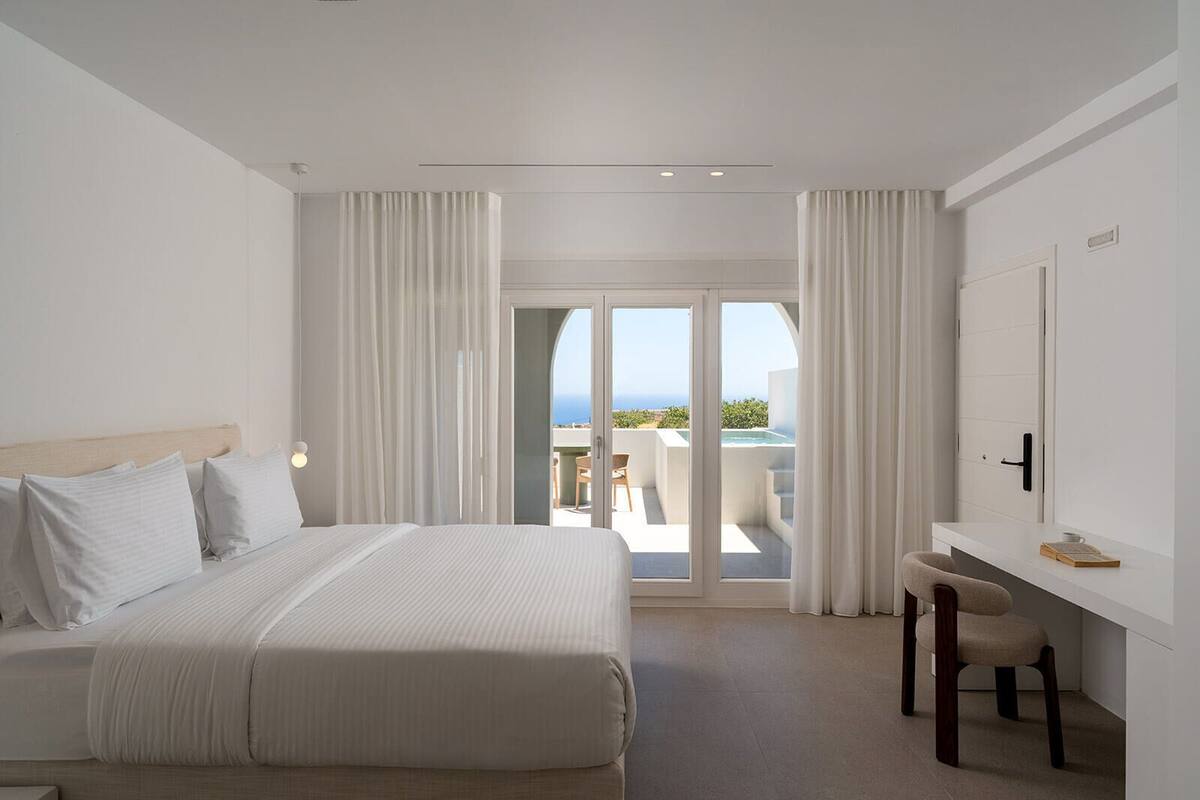 A hotel room with a bed, a desk, a chair, and a view of the sea.