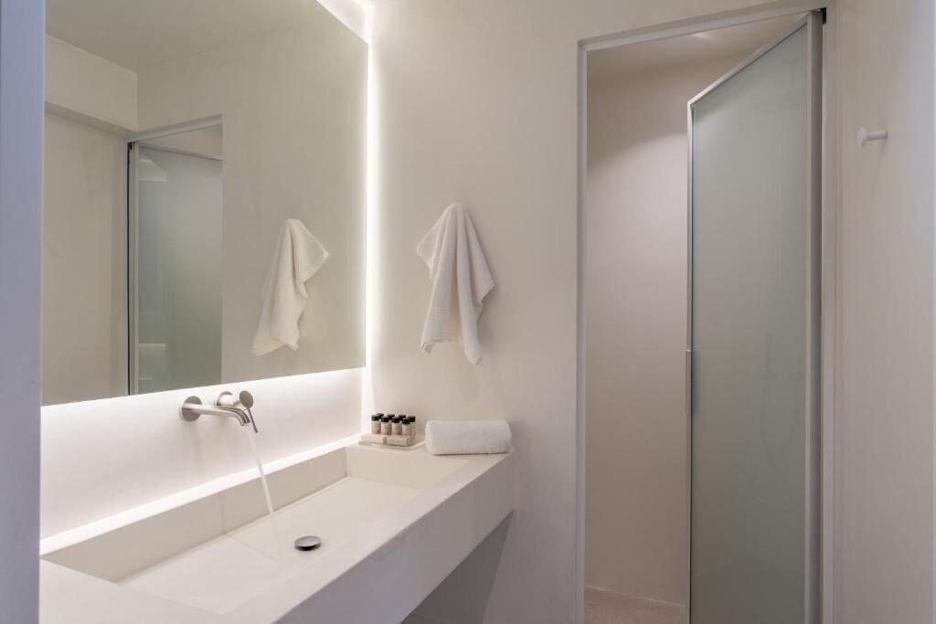 Un baño moderno con un espejo grande, un lavabo blanco y una cabina de ducha de vidrio.