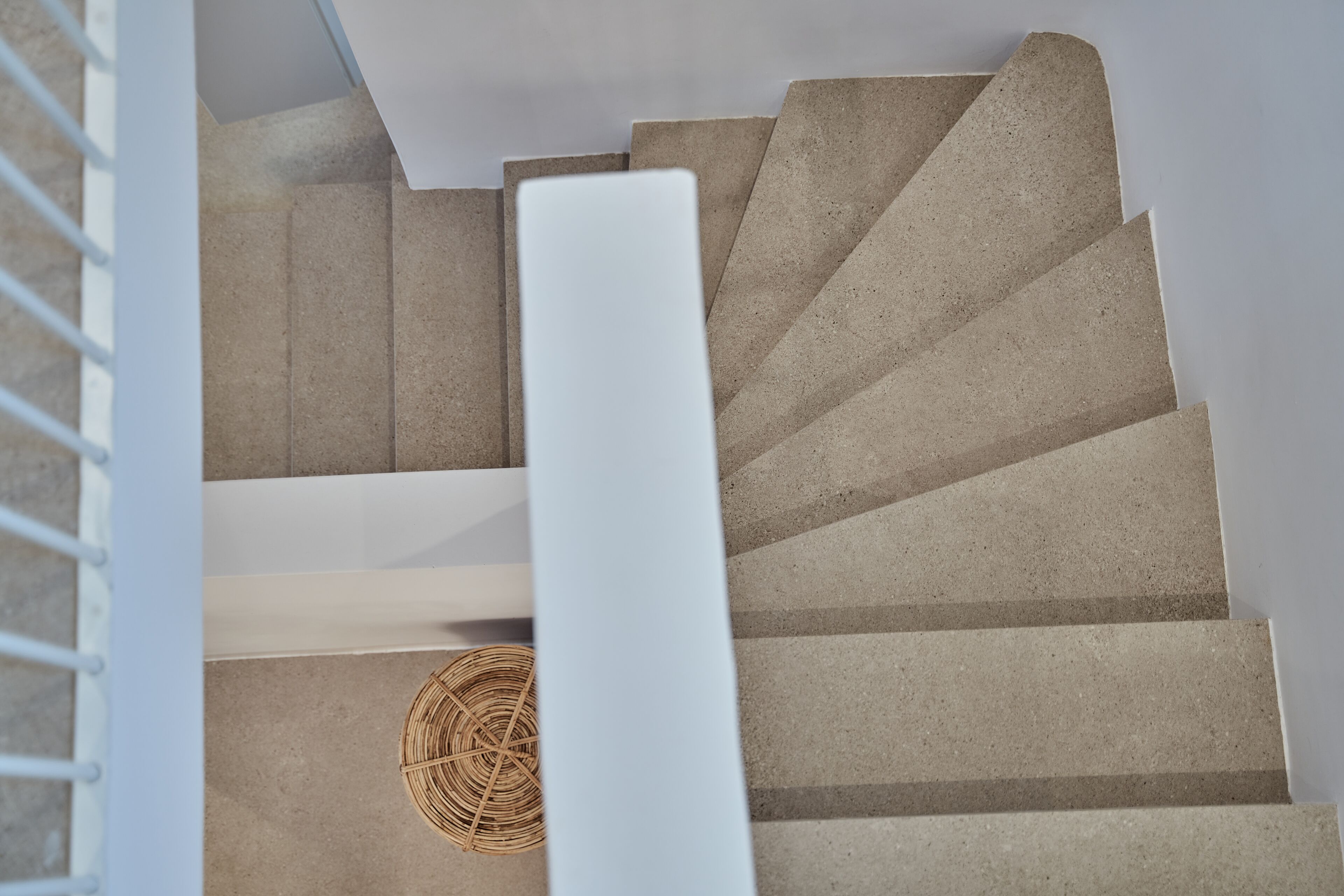 A spiral staircase with beige steps and a white handrail.