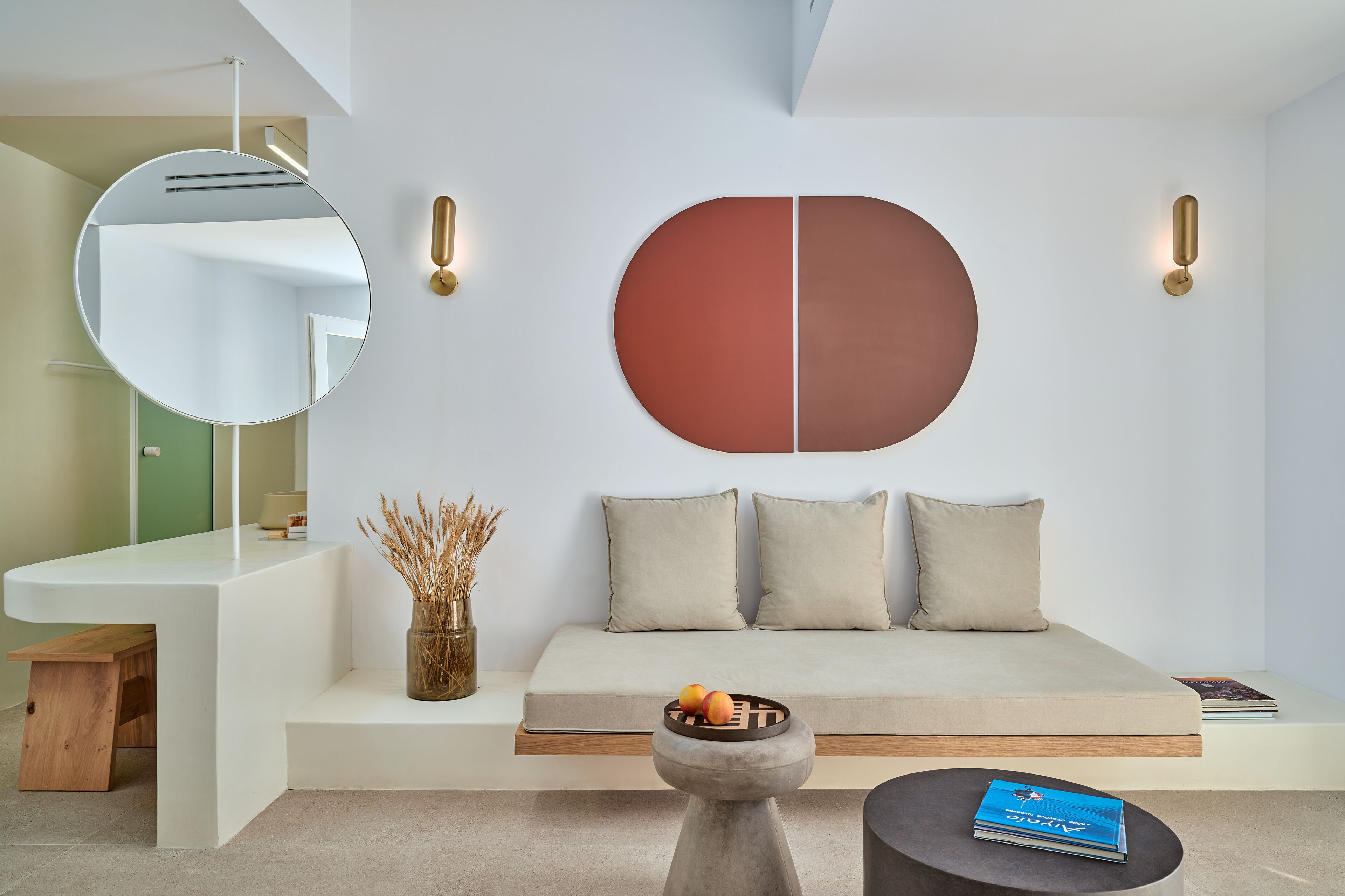 A modern living room with a sofa, a round mirror, a round table with a book, and a wall-mounted light fixture.