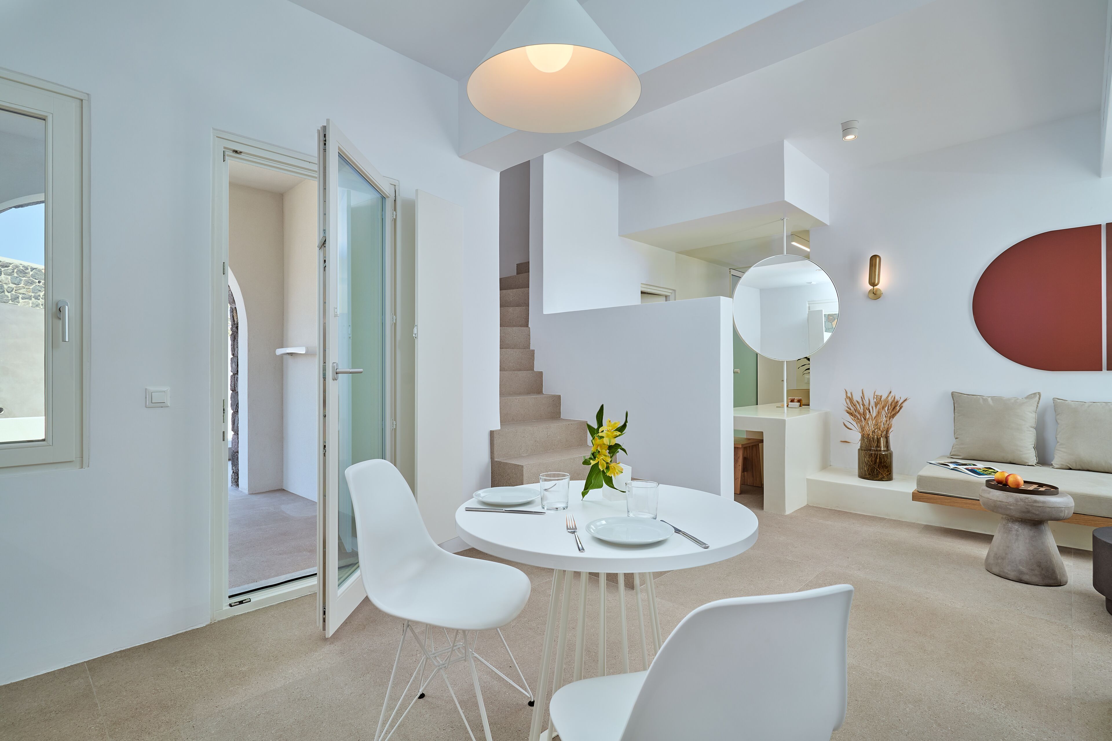 Et moderne interiør med et rundt spisebord, hvide stole, en trappe og minimalistisk indretning.