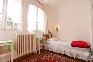 Ein Schlafzimmer mit einem Bett, einem Nachttisch, einem Heizkörper und einem Fenster mit Vorhängen.