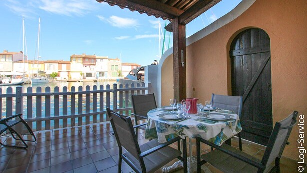 A terrace with a table set for dining, overlooking a canal with boats.