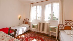 A small, cozy room with two single beds, a wooden chair, a small table, and a radiator.