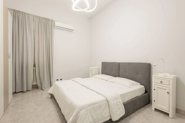 A bedroom with a bed, a nightstand, a bedside table, a wardrobe, and a ceiling light fixture.