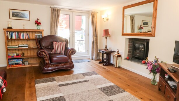 A living room with a leather armchair, a bookshelf, a fireplace, and a large mirror. - Blackbird Cottage (Telford)