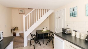 A compact kitchen with a dining area, a staircase, and a white door. - Blackbird Cottage (Telford)