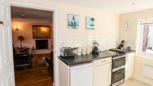 A compact kitchen with a stove, oven, and toaster. There is a dining area with a couch and a lamp. - Blackbird Cottage (Telford)