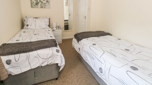A bedroom with two beds, a bedside table, a mirror, and a painting on the wall. - Blackbird Cottage (Telford)