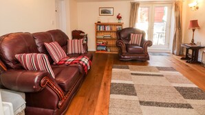 A living room with a brown leather sofa, a striped armchair, a bookshelf, and a patterned rug. - Blackbird Cottage (Telford)
