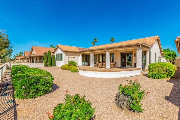 A two-story house with a covered patio, surrounded by well-maintained gardens and palm trees.