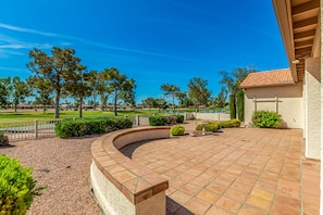A covered patio area with a curved stone border, a pool in the background, and a view of a golf course.