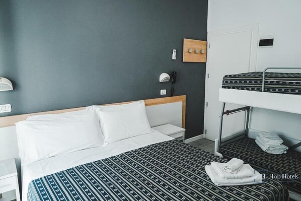 A hotel room with a single bed, a bunk bed, a bedside table, a lamp, and a wall-mounted phone. - NAUTIC BEACH HOTEL (Rimini)