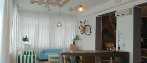 A living room with a sofa, a dining table, chairs, and a bicycle mounted on the wall.