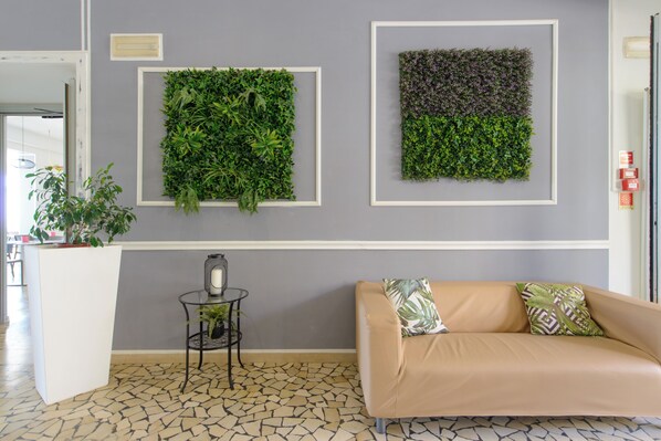 Un espace d’accueil comprenant un canapé, une petite table avec une plante, et deux jardins verticaux encadrés accrochés au mur.