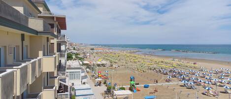 A coastal hotel with balconies overlooking the beach, a children's play area, and a view of the sea.