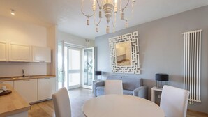 A modern kitchen with white cabinets, a dining table with chairs, a chandelier, and a gray sofa in a bright living area. - Don Onofrio Holiday House - app.to Domitilla (Monopoli)