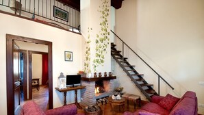 A living room with a fireplace, two purple sofas, a TV on a wooden table, and a staircase. - Tenuta di Forte Sorgnano | Farmhouse with private pool (Gualdo Cattaneo (PG))