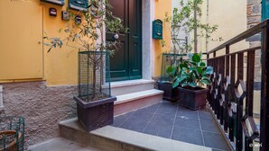 Un callejón estrecho con un edificio amarillo, una puerta verde y plantas en macetas.