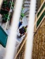 A narrow alleyway with stone walls, potted plants, and a person climbing a wall.