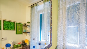 Un baño con espejo, paredes verdes, un lavabo y una ventana con cortinas estampadas.