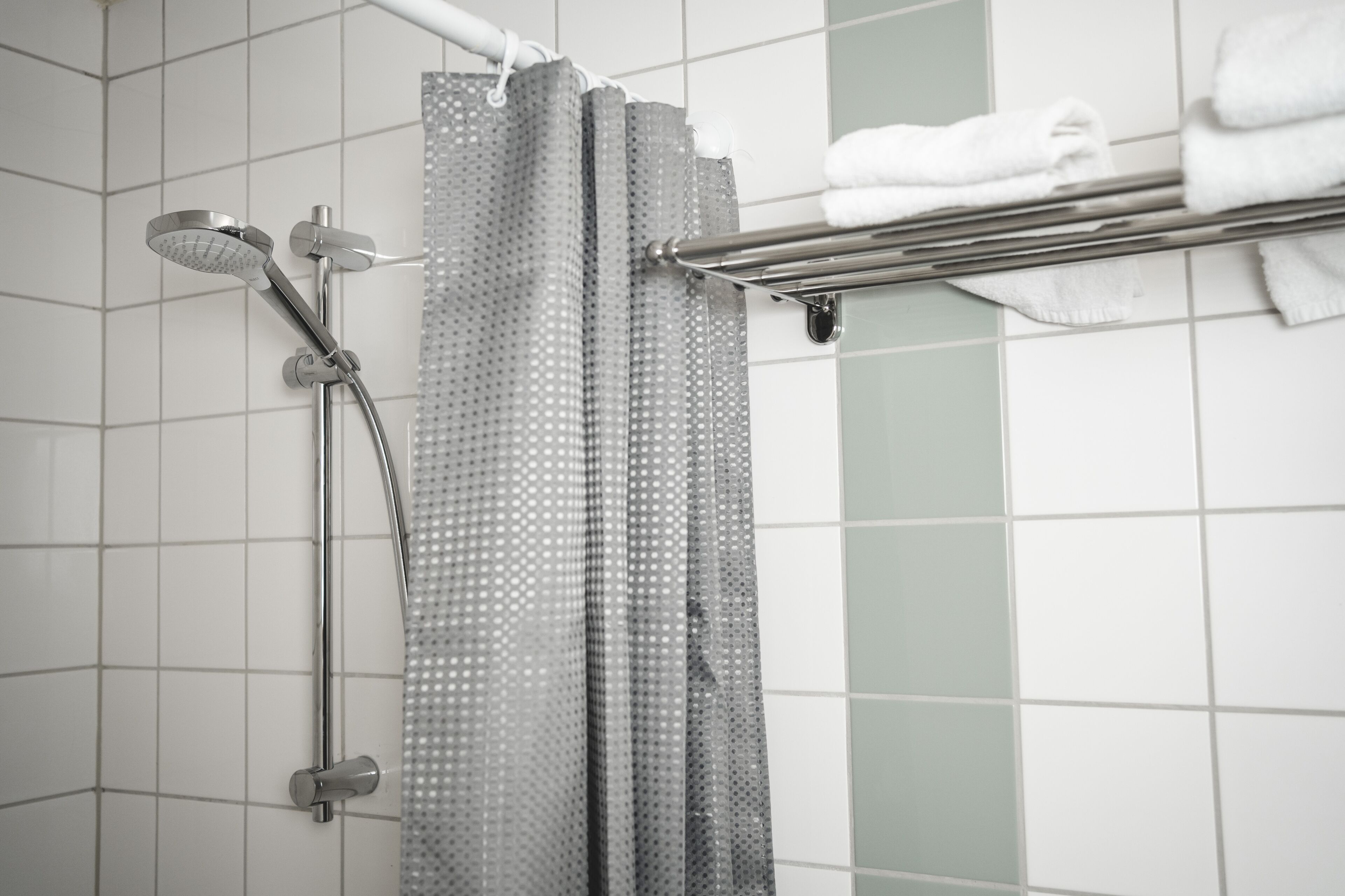 A bathroom with a shower, a towel rack with folded towels, and tiled walls.