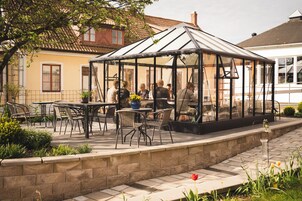 Et drivhus af glas med borde og stole, omgivet af en stenvæg og planter.