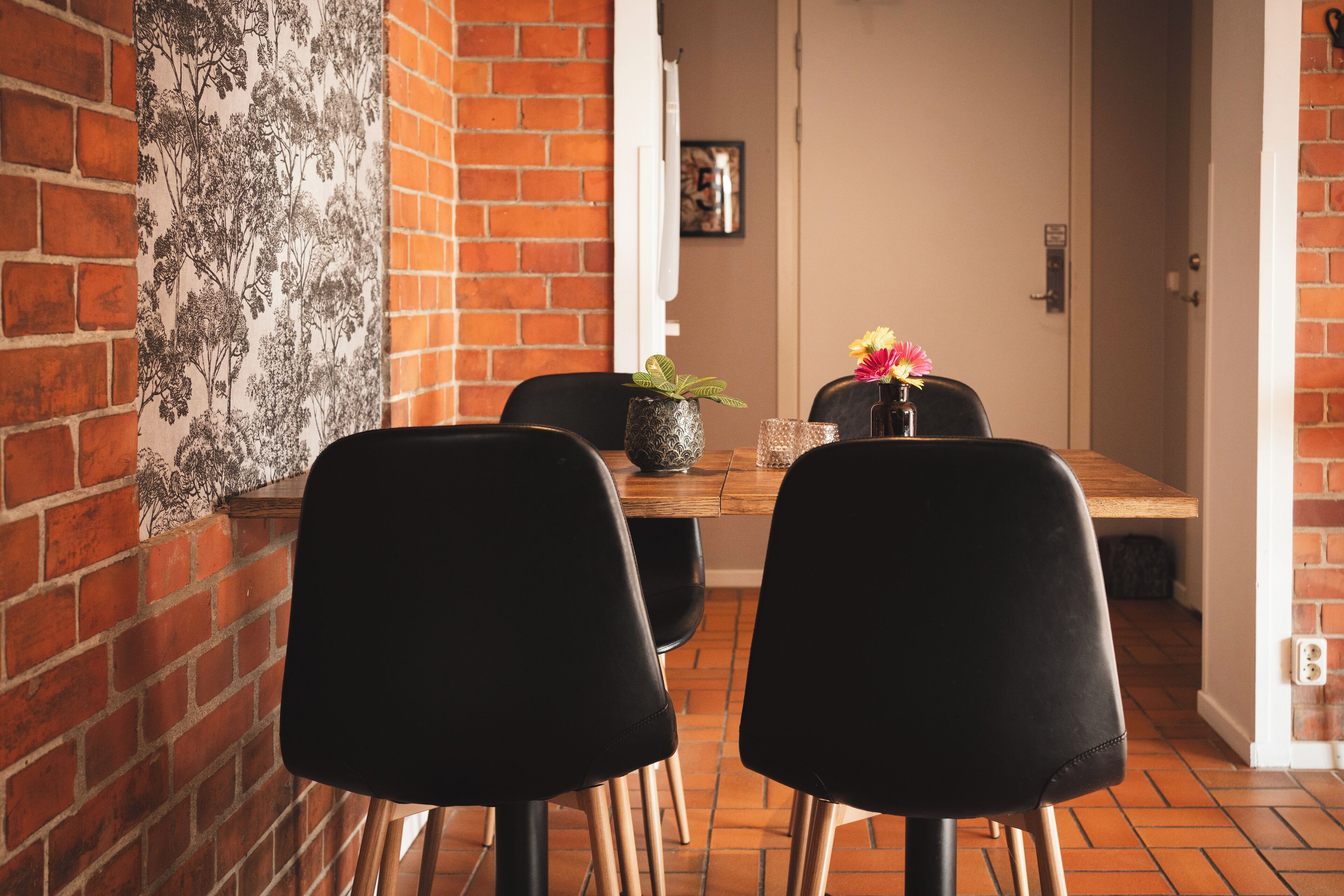 A dining area with a brick wall, a wooden table, and black chairs.