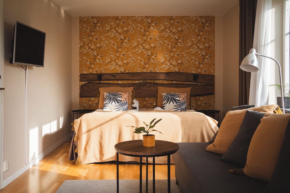 A bedroom with a bed, a small table with a plant, and a TV mounted on the wall.