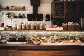 Una encimera de cocina con diversos alimentos y utensilios de cocina. Hay frascos con alimentos en conserva, un bol de fruta y una botella de salsa.