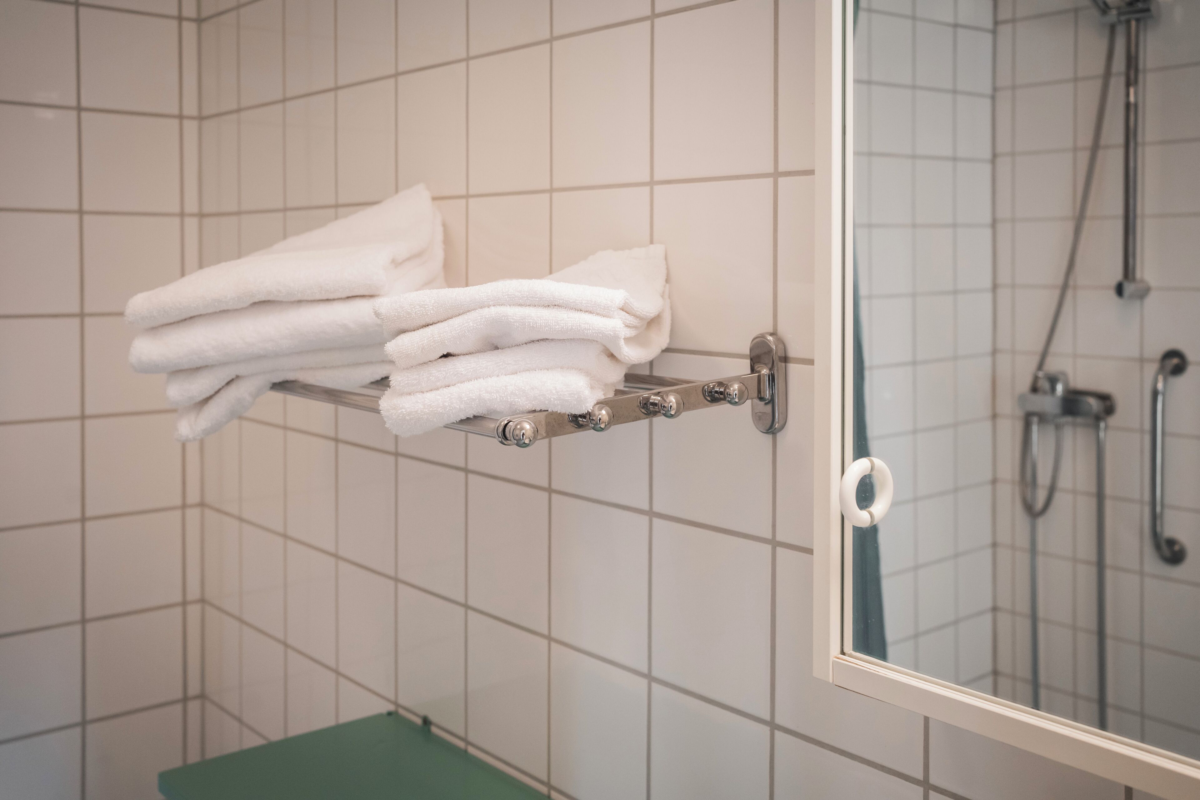 Un bagno con un portasciugamani pieno di asciugamani piegati, una doccia e uno scaffale verde.